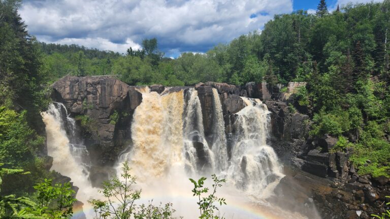 A vibrant rainbow arcs over a cascading waterfall, creating a stunning natural scene in the sky.