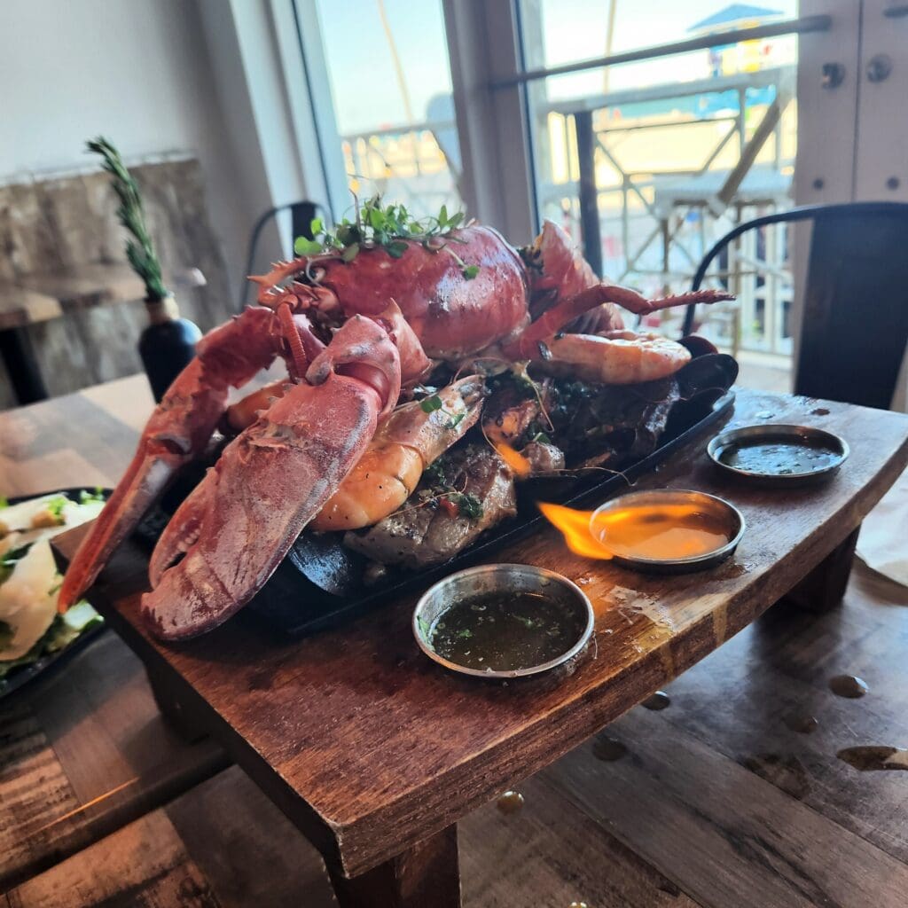 A large lobster rests on a wooden table beside a bowl of food.